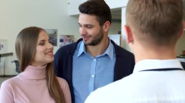 Yakışıklı esmer partneri ona hayranlıkla bakarken şık bir beyaz kadın şık bir satıcıdan arabanın anahtarlarını alırken heyecanla ışıldıyor. Modern bayilik ayarı enerji ile uğulduyor, gösterişli lüks otomobiller ve