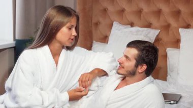 Büyüleyici bir çift, lüks beyaz bornozlara sarılı, rahat bir otel odasında dinleniyor. Muhteşem kadın gülümsüyor ve erkek arkadaşıyla samimi bir konuşma yapıyor. Sevgi ve bağ dolu sıcak bir ortam yaratıyor.