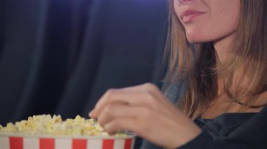 Orta yaşlı beyaz bir kadın sinemada keyifli bir andan zevk alıyor, canlı çizgili patlamış mısır kovasına uzanıyor. Kahverengi saçları usulca dökülüyor tereyağlı atıştırmalıklara daldıkça, sinemanın ve boş zamanların neşesini somutlaştırıyor.