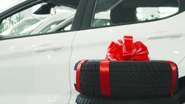 Koyu renk saçlı neşeli bir adam güzel sarılmış yeni tekerleklerin yanında oturuyor, canlı kırmızı bir fiyonk sergiliyor. Sıcak gülümsemesi heyecan saçıyor. Seyircileri bu otomotiv hediyesinin heyecanını paylaşmaya davet ediyor.