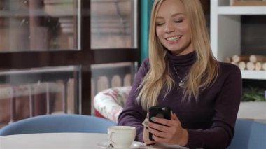 Hoş bir kafede cep telefonuyla mesajlaşırken uzun sarı saçlı neşeli bir genç kadın gülümsüyor. Yumuşak bir ışık ve dumanı tüten bir fincan kahveyle, sıcak ortam, onun keyifli bağlanma anını güçlendirir.