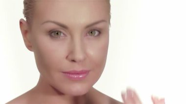 Beyaz arka planda kusursuz cildine krem süren beyaz bir kadının çarpıcı portresi. Taze, parıldayan teni ve narin dokunuşu saflık ve kendine bakımı çağrıştırıyor, cilt bakımı ayinlerinin güzelliğini vurguluyor.