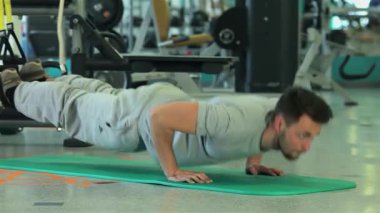 Orta Doğu kökenli kararlı genç bir adam modern bir spor salonundaki canlı yeşil bir paspasın üzerinde güçlü bir şınav çekiyor. Odaklanmış ifadesi ve kaslı fiziği fitness ve dayanıklılık eğitimine olan bağlılığını vurguluyor.