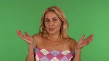 Çekici, olgun, dalgalı sarı saçlı bir kadın şaşırmış görünüyor, elleri canlı yeşil bir kromakey arka planına karşı neşeli bir jest olarak kaldırılmış. Bu büyüleyici portre şaşkınlık ve duygunun özünü yakalar, izleyicileri bağlanmaya davet eder.