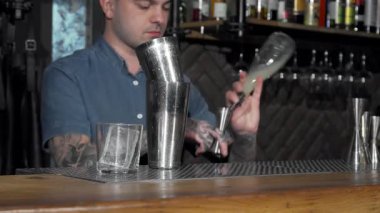 Dövmeli bir barmen şık bir barda canlı bir kokteyl hazırlar ve miksoloji yeteneklerini sergiler. Renkli içeceği bardağa dökerken atmosfer elektriklidir. Gece hayatını yansıtan bir dizi içki şişesiyle çevrilidir.