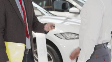 Parlak ve modern bir galeride, bir adam yeni arabasının anahtarlarını alırken güvenle bir satıcının elini sıkar. Bu an, bir aracı satın alma yolculuğundaki güven ve ortaklığı sembolize eden bir anlaşmanın heyecanını yakalıyor.