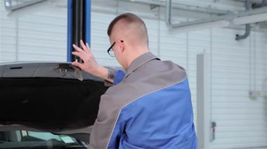 Mavi üniformalı kendini işine adamış genç bir tamirci ustalıkla kaputu kapatıyor ve zanaatkarlığını sergiliyor. Elinde bir tebessüm ve bezle, bu sarışın Kafkas profesyonel parlak, modern bir garajda otomotiv mükemmelliğinin ruhunu temsil ediyor.