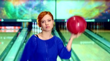 Canlı kızıl saçlı bir kız bowling salonunda kendinden emin bir şekilde dönüyor. Bowling topu başının üstünde duruyor. Bu enerjik, mavi bir süveter giyen beyaz kadın, baloyu bırakmaya hazırlanırken yeteneğini ve hevesini sergiliyor.