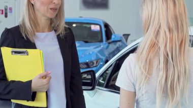 Hevesli bir bayan müşteri şık bir galeride hazır bir satış elemanından memnuniyetle araba anahtarı alır. Bu canlı sahne başarılı bir alışverişin özünü yakalar, çarpıcı bir arkaplan arasında yeni sahipliğin heyecanını vurgular.