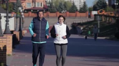 Dinamik bir ikili canlı bir şehir manzarası boyunca, ferahlatıcı sonbahar havasını kucaklayarak yan yana koşu yapar. Atletik kıyafetleri ve neşeli ifadeleri spor ve sağlıklı bir yaşam tarzına olan bağlılıklarını yansıtıyor. Bu sahneyi mükemmel bir temsil ediyor.