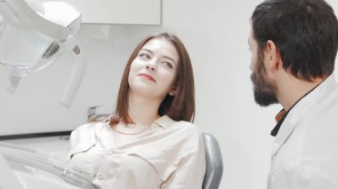 Çekici genç bir kadın modern bir diş kliniğinde dişlerini inceleyen yetenekli bir dişçi gibi rahatlıyor. Parlak, steril çevre diş hijyen ve bakımının önemini vurgular, hastalara sağlıklı bir gülümseme ve dişçilere özen gösterir.