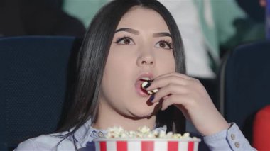 Asyalı bir kız, bir kova patlamış mısırı yerken film karşısında büyülenmiş bir şekilde rahat bir sinema koltuğunda oturuyor. Arkadaşlar ve çiftler bu zevkli film deneyimini paylaşırken, hareketli atmosfer kahkaha ve heyecanla doludur.