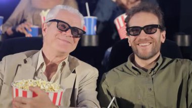 Samimi bir sinemada, gri saçlı ve orta yaşlı bir adam üç boyutlu bir filme dalmışken aynı kahkahayı paylaşıyor. Neşeli atmosfer patlamış mısır dolu kovalarıyla güçlenir ve arkadaşlar arasında hoş bir bağ kurma anı yaratır.