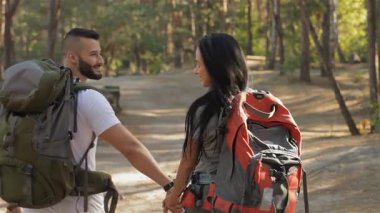 Bir çift romantik yürüyüşçü, yükselen ağaçlarla çevrili güneşli bir orman yolu boyunca el ele yürürler. Çekici beyaz erkek ve kadın, açık hava maceralarının neşesini kucaklarken, aşklarını ve ilişkilerini somutlaştırırken gülümsüyorlar.