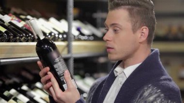 Keskin gözlü şık bir genç adam ahşap raflardaki etkileyici şarap çeşitleriyle çevrili bir şişe şarabı inceliyor. Odaklanmış ifadesi ve şık kıyafeti kaliteye olan tutkuyu yansıtıyor. Bu anı mükemmel bir karışım haline getiriyor.