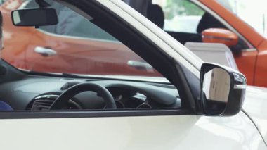 Çekici bir gülümsemesi olan neşeli genç bir adam yepyeni arabasında güven içinde oturuyor, heyecan ve gurur gösteriyor. Canlı bayilik arkaplanı kutlama ve başarı atmosferini yükselterek, yeni sahipliğin heyecanını vurguluyor