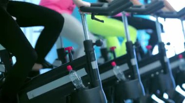 Dört enerjik kız arkadaş hareketsiz bisikletlerle pedal çeviriyor, canlı bir spor salonunda zindelik ve sağlığa bağlılıklarını sergiliyorlar. Renkli spor kıyafetleri ve odaklanmış ifadeler, onların arkadaşlığını ve kararlılığını vurgular.