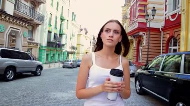 Güzel genç bir kadın, elinde bir bardak tutarak zarif bir şekilde eski bir kasabada yürüyor. Parlak mimarisi ve kaldırım taşı sokakları yaz macerası için harika bir zemin oluşturuyor, neşe ve merak saçıyor.