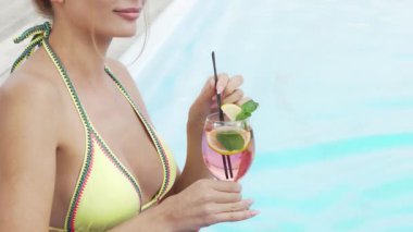 Büyüleyici bir kırpma sahnesinde canlı bikinili güzel bir kadın ışıldayan havuzun yanında ferahlatıcı bir kokteyl yudumluyor. Sahne, yaz havası yayıyor. Sıcak güneşin altında rahatlamaya ve keyif almaya davetiye çıkarıyor.