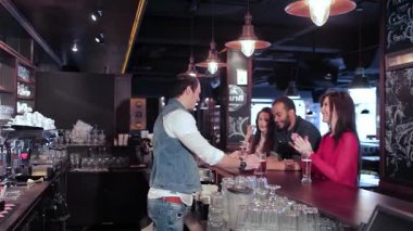 Canlı bir üçlü, iki neşeli kız ve bir erkek, sıcak bir ışık ve canlı bir atmosferle çevrili, hareketli bir barda içkilerini sabırsızlıkla bekliyorlar. Kahkahaları havayı dolduruyor. Arkadaşlıklarını kutluyorlar. Eğlencenin ve futbolun tadını çıkarıyorlar.