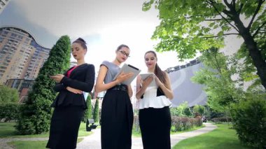 Canlı bir şehir parkında, üç kendine güvenen iş kadını bir tablet üzerinde çalışırken canlı bir tartışmaya girişirler. Şık kıyafetleri ve ışıl ışıl gülümsemeleri takım çalışmasının ve başarının dinamik atmosferini yansıtıyor.
