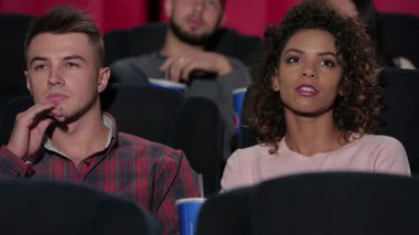 Lüks tiyatro koltuklarına kurulmuş genç bir çift, film izlerken keyifli bir anı paylaşıyorlar. Sinema izleyicileri tarafından çevrelenmiş, patlamış mısır ve sodanın tadını çıkarıyorlar, sinematik bir deneyimin heyecanı ve sıcaklığını somutlaştırıyorlar.