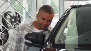 Neşeli bir Afrikalı genç adam modern bir galeride yeni arabasının yanında araba anahtarlarını tutarken gururla ışıldıyor. Bu canlı sahne, araba sahibi olmanın heyecanını yansıtıyor. Açık yollardaki özgürlük ve macerayı simgeliyor.