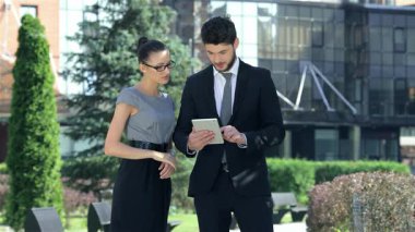 Kendinden emin bir işadamı ve başarılı bir iş kadını canlı bir şehir ortamında bir tableti incelerken canlı bir tartışmaya girişirler. Mesleki kıyafetleri ve hareketli ifadeleri, hedeflerine ulaşmada ortak bir kararlılığı yansıtıyor.