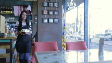 Işıl ışıl gülümseyen genç bir garson rahat bir kafede hazır bekliyor. Şık bir önlük giyer, neşeyle siparişleri alır. Bu arada taze demlenmiş kahvenin davetkar kokusu havayı doldurur ve sıcak bir atmosfer yaratır.