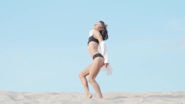 Göz kamaştırıcı uzun bir çekim, siyah bir bikiniyle zarif bir şekilde dans eden, hareketlerini akıcı ve yumuşak çöl kumu üzerinde ifade eden muhteşem bir kadını yakalar. Bu büyüleyici sahne kadınlığı ve şehveti yansıtıyor, dansçıları sergiliyor.