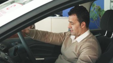 Koyu renk saçlı bir adam sürücü koltuğunda rahatça oturur, direksiyonu tutarken şakacı bir şekilde tuşlara basar. Sıcak gülümsemesi heyecan saçıyor. Seyircileri bu modern otomobili keşfetme heyecanını paylaşmaya davet ediyor.
