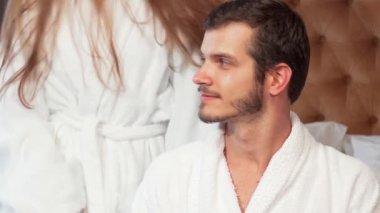 Neşeli bir çift balayı süitlerinde kucaklaşır ve kameraya gülümserken mutluluk saçar. Güzel genç kadın ve kocası, her ikisi de lüks bornozlar içinde, sevgi ve rahatlıkla dolu, mükemmel bir ortam yaratıyorlar.