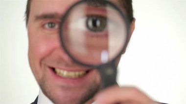 Kendinden emin genç bir işadamı büyüteçten bakarken gülümser ve detaylara olan yoğun ilgisini vurgular. Bu ilgi çekici görüntü, iş dünyasındaki kararlılık ve merakın özünü yakalar,