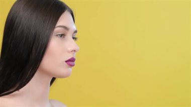 Çekici bir Asyalı kadın zarif bir şekilde parlak sarı bir arka plana karşı poz veriyor. Parmağı hafifçe erik dudaklarına bastırılarak neşeli bir sessizlik hareketi yapıyor. Omuzlarından süzülen uzun, parlak saçlarıyla cazibe ve cazibe saçarak izleyicileri davet ediyor.