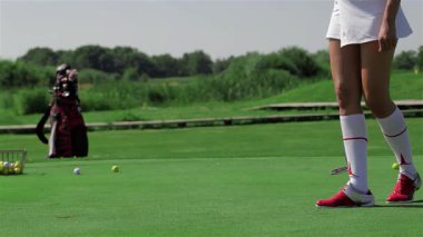 Beyaz kıyafetli, çarpıcı bir kızıl saçlı genç beyaz bir kadın yemyeşil golf sahasında diz çöküp deliğe dikkatle çalışıyor. Atletik duruşu ve konsantrasyonu, bir sonraki vuruşunu yapmaya hazırlanırken oyuna olan tutkusunu yansıtıyor.