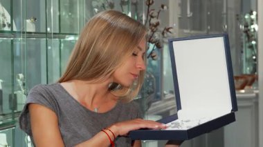 Neşeli bir kadın zarif bir butikte zarif bir mücevher sergilerken kameraya ışık saçıyor. Lüks parçalar hafif ışıklandırma altında parıldıyor. Potansiyel alıcıları ustalığın güzelliğine kendilerini kaptırmaya çağırıyorlar.