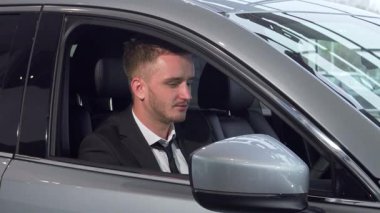 Düzgün bakımlı sakallı neşeli bir işadamı yeni arabasında, gururla elinde anahtarlarla oturuyor. Bu canlı sahne, sahipliğin heyecanını ve modern bir otomobili sürmenin heyecanını yansıtıyor, başarıyı simgeliyor ve