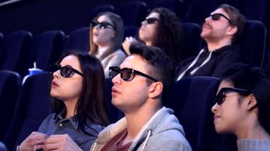 Genç yetişkinlerden oluşan çeşitli bir grup, rahat bir sinemada 3 boyutlu heyecan verici bir filme hayran kalıyor. Sarışın adam ekranı heyecanla işaret ederken Asyalı kadın sinema büyüsüyle meşgul olarak öne doğru eğiliyor.