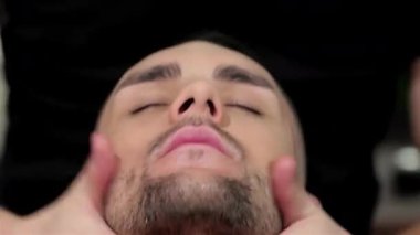 Yetenekli bir berber, şık bir berber dükkanında müşterinin yüzüne nazikçe masaj yapar ve rahatlamasını sağlar. Atmosfer klasik cazibeyle dolu, modern erkekler için bakım ve özgüven sanatını sergiliyor.