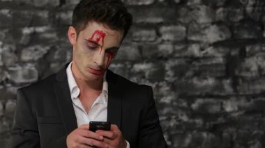 Gösterişli siyah takım elbiseli, çarpıcı bir erkek vampir siyah duvarlara karşı akıllı telefon kullanıyor. Dramatik makyaj ve kana benzer çizgilerle vurgulanan solgun yüzü, ürkütücü bir Cadılar Bayramı havası yaratıyor, modern teknolojiyi harmanlıyor.