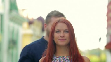 Sakallı bir adam ve kız arkadaşı, akşam ışığının sıcacık parıltısıyla yıkanmış, eski güzel kasabada dolaşırken şefkatli bir öpücük paylaşıyorlar. Neşeli ifadeleri ve günlük kıyafetleri kaygısız bir yaz macerasını yansıtıyor.