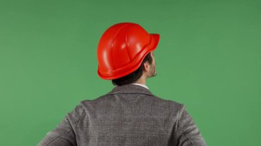 Çarpıcı kırmızı şapkalı bir erkek müteahhit, parlak yeşil renkli bir ekranı inceliyor. Bu görüntü, inşaat endüstrisindeki yeniliğin ve profesyonelliğin özünü yansıtıyor. Yetenekli bir mimarı gözler önüne seriyor.