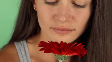 Uzun, dalgalı saçları olan güzel bir kadının büyüleyici portresi canlı kırmızı bir çiçeğin tatlı kokusunu taze yeşil renkli bir arka planda neşeyle soluyor. Onun sakin ifadesi ve nazik gülüşü pozitiflik ve sükunet saçıyor.