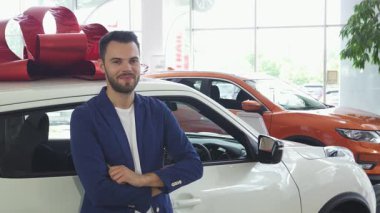 Şık genç bir adam neşeyle ışıldar, araba anahtarlarını gösterirken yepyeni arabasına yaslanır ve şenlikli bir fiyonk takar. Bu canlı sahne sahipliğin heyecanını ve yoldaki yeni maceraların heyecanını yakalıyor.