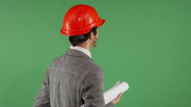 Sert şapkalı bir erkek mühendisin dinamik arka görüntüsü canlı yeşil bir ekrandaki nesneleri ustalıkla manipüle ediyor. Bu sahne, modern teknolojinin ve mühendislik alanındaki yeniliklerin özünü yansıtıyor.