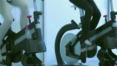 Canlı bir spor salonu ortamında, iki genç bayan spor bisikletleriyle pedal çevirirken neşeli bir anı paylaşıyor, gülümsemeleri pozitiflik ve dostluk saçıyor. Sahne fitness ve arkadaşlığın özünü yakalıyor, atletik figürlerini ve...