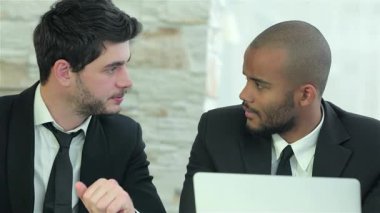 Birinin siyah saçlı, diğerinin de bakımlı sakallı iki kendine güvenen genç işadamı, düzgün bir dizüstü bilgisayardaki bilgileri analiz ederken derin bir sohbete dalıyorlar. İfadeleri kararlılığı ve işbirliğini yansıtıyor.