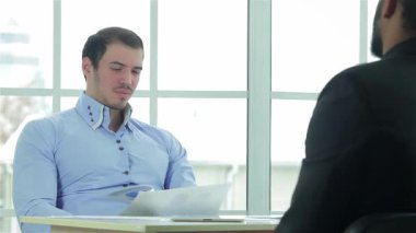 İki kendine güvenen iş adamı şık bir müzakere masasında, belgeleri analiz ederek ve bir iş planı üzerinde işbirliği yaparak dinamik bir tartışmaya girişirler. Keskin resmi giysiler içinde profesyonellik ve kararlılık yayıyorlar. Güneş ışığı parlıyor.