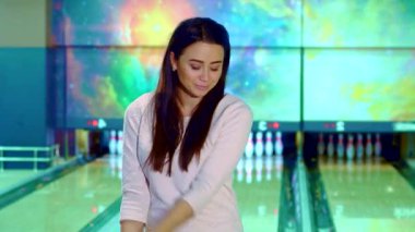 Neşeli genç Asyalı bir kadın canlı pembe bir bowling topu tutuyor, kendine güven ve heyecan saçıyor. Renkli bir kozmik arkaplanda, bovling sahasında duruyor, oyunun heyecanını somutlaştırıyor.