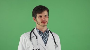 Gıcır gıcır beyaz önlüklü neşeli genç bir erkek doktor sıcak bir gülümseme sergiliyor, kendine güven ve yakınlık yayıyor. Boynunda bir steteskop ile, hayat dolu yeşil bir krom arka plana karşı duruyor, sağlık hizmetinin ruhunu ve